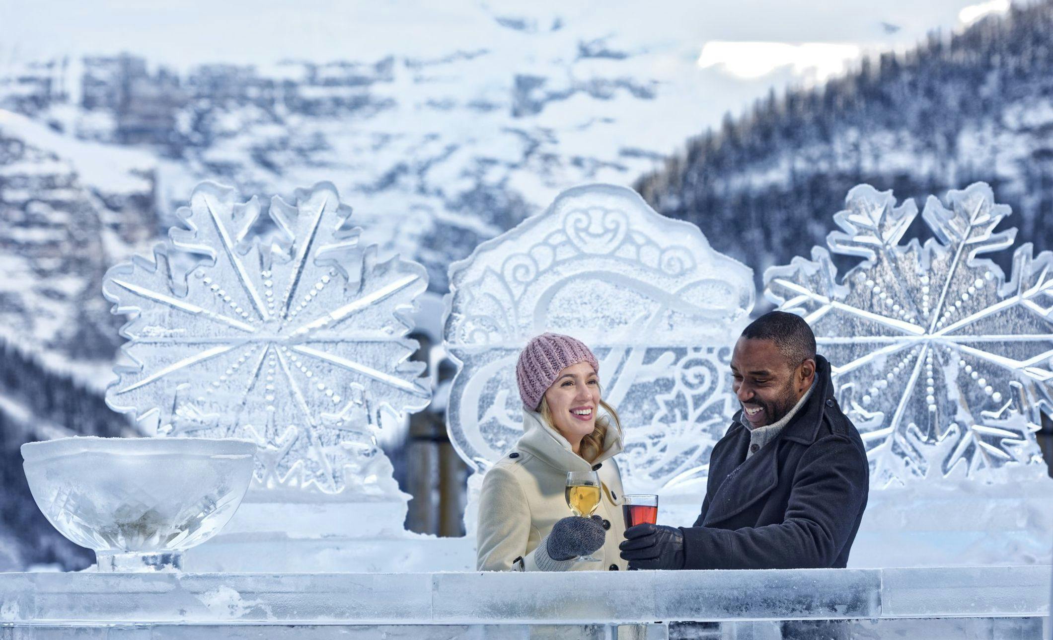 A couple enjoying a drink at an ice bar against a snowy backdrop