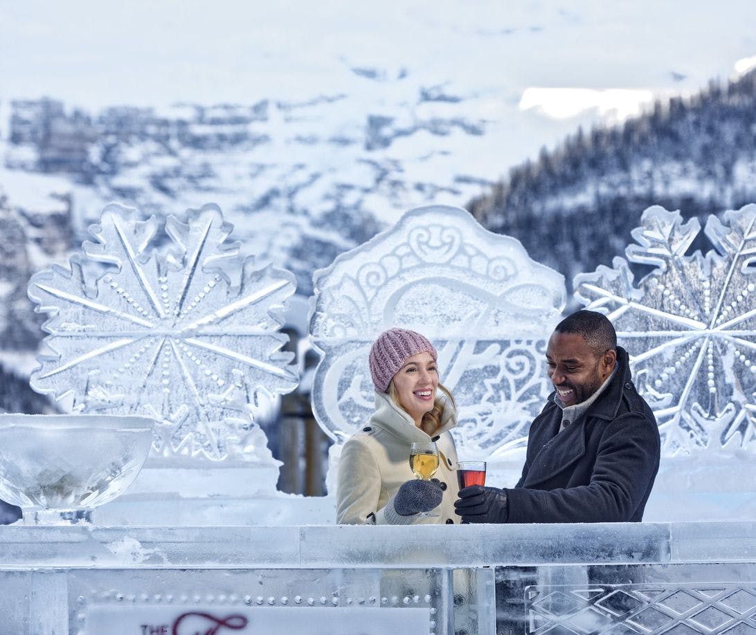 A couple enjoying a drink at an ice bar against a snowy backdrop