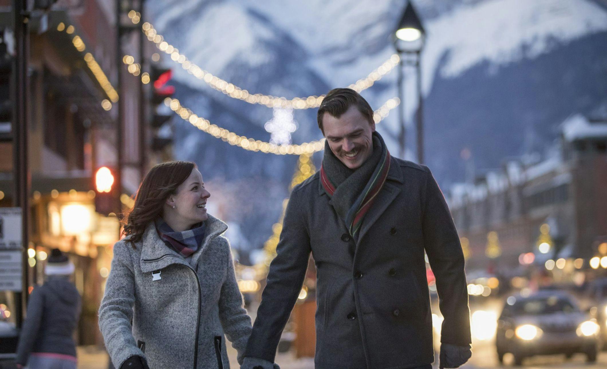 A couple walking downtown in the winter with Christmas lights in the background