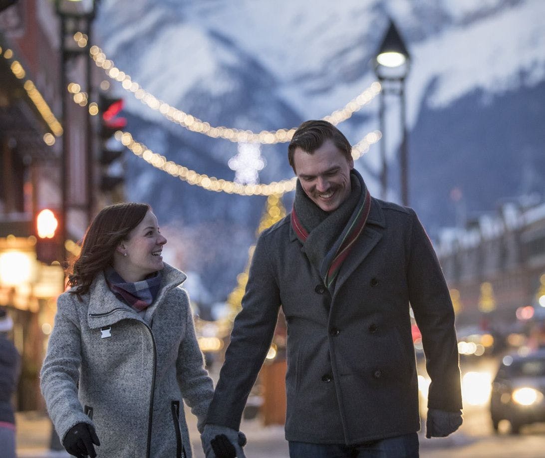 A couple walking downtown in the winter with Christmas lights in the background