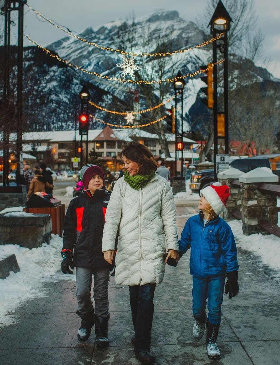 A family walking down Banff Avenue with Christmas lights and mountains behind them