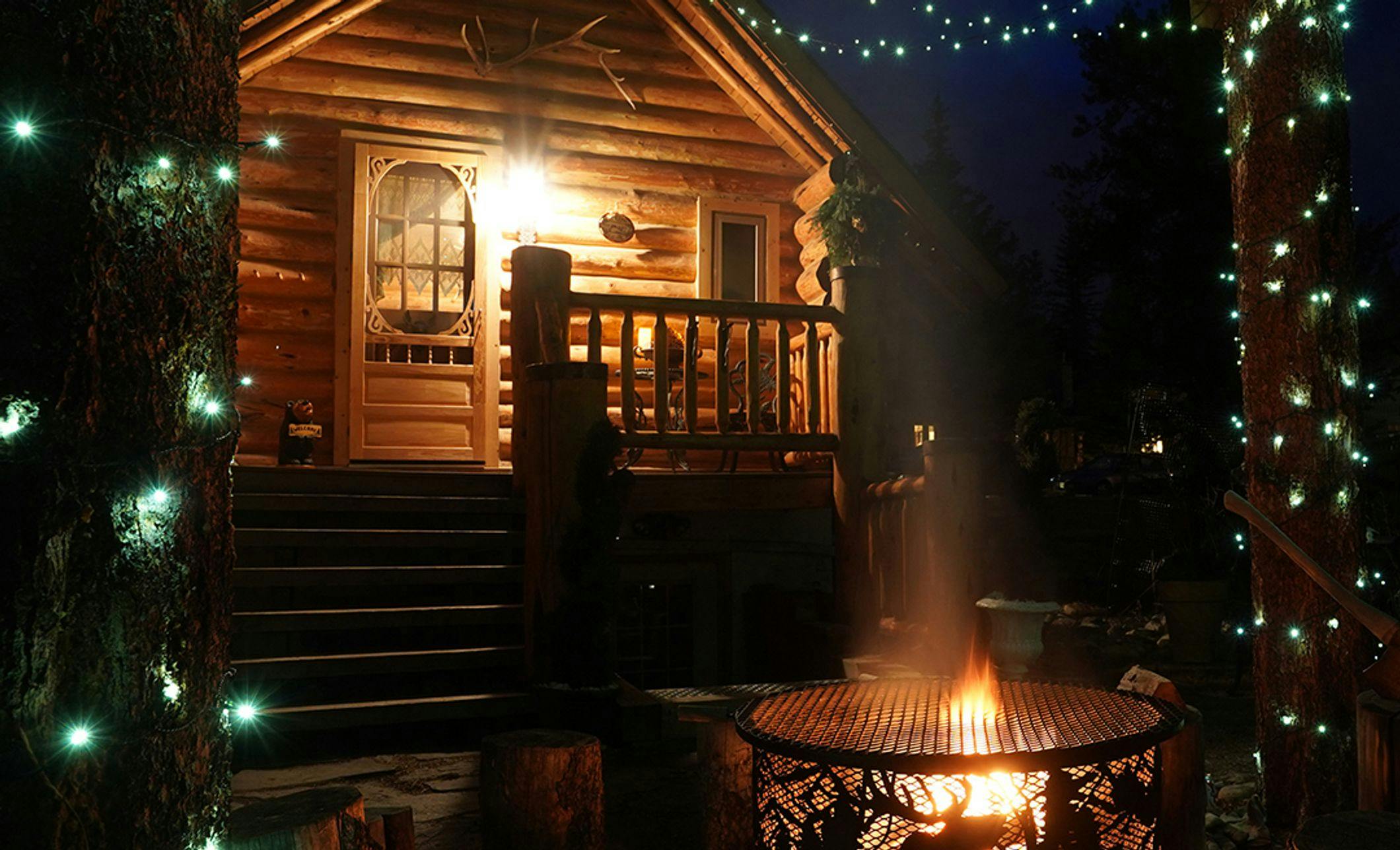 Log cabin with Christmas lights and a burning outdoor fire