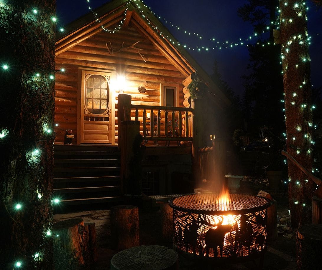 Log cabin with Christmas lights and a burning outdoor fire