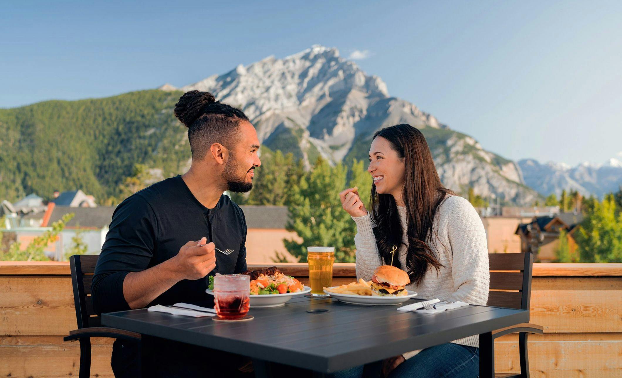A couple enjoys lunch on a sunny rooftop patio with a mountain framing their table in the background