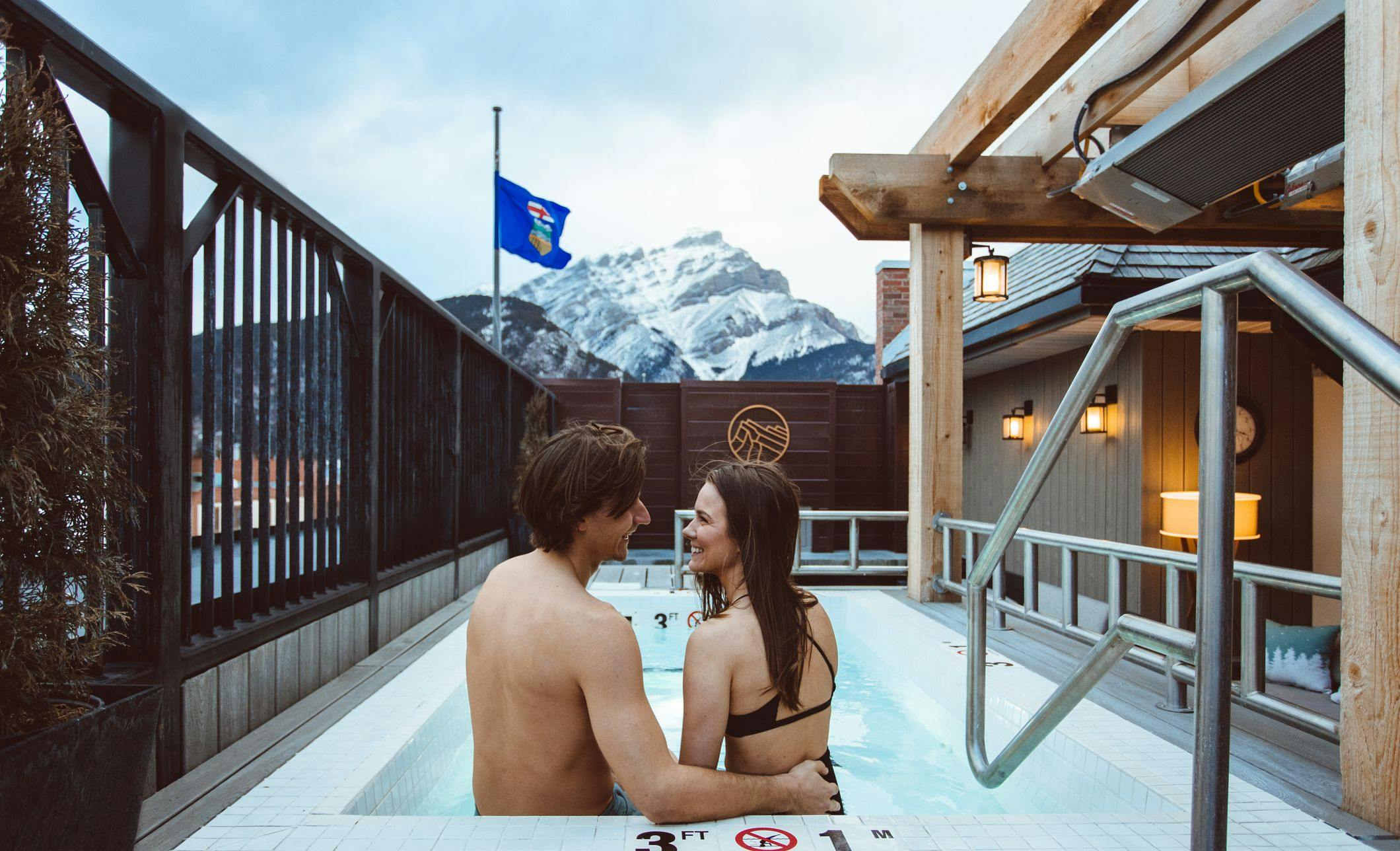 A couple laughing in an outdoor hot tub with a snow covered Cascade Mountain in the background