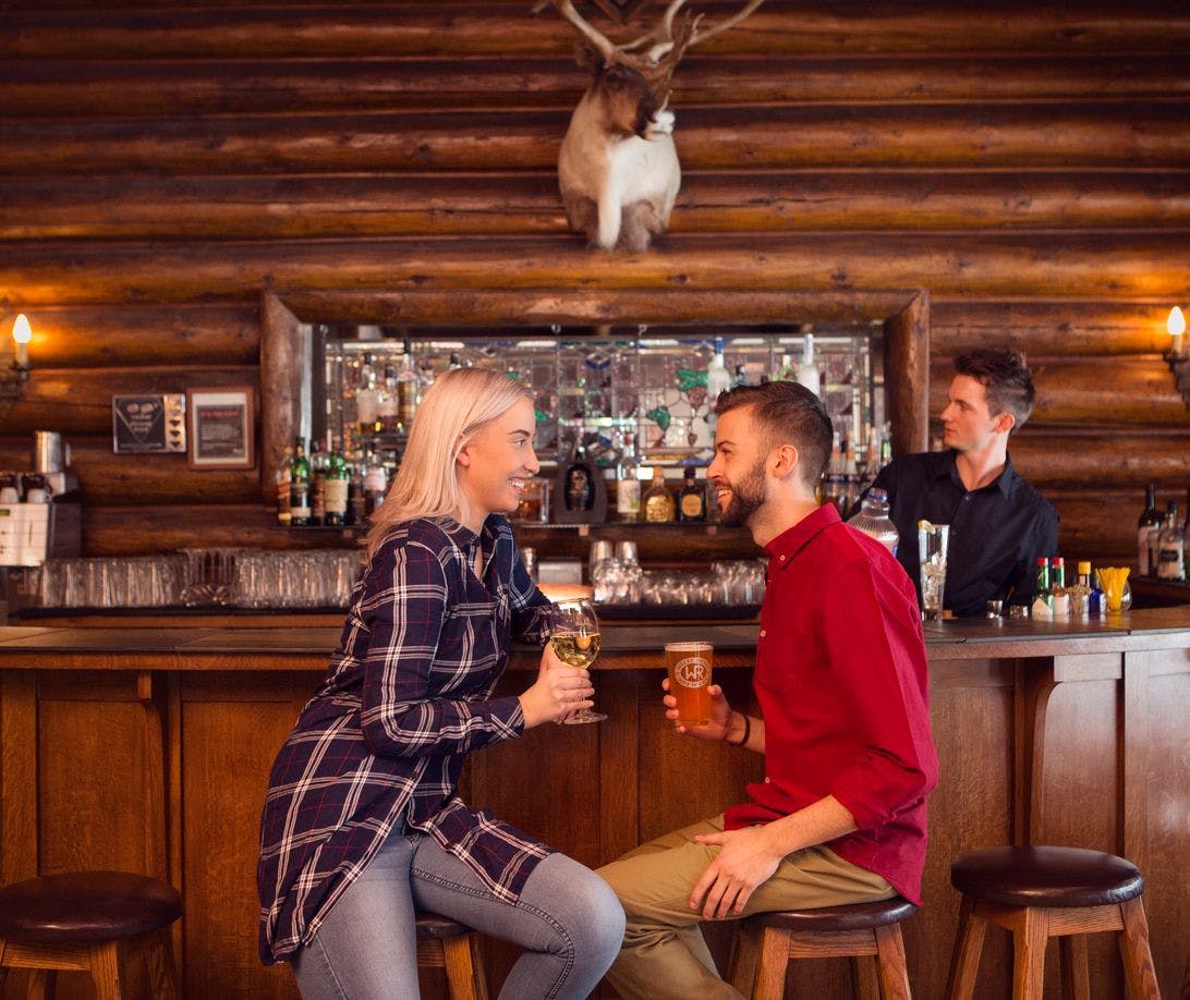 A couple sitting at a rustic bar with a glass of wine and a beer