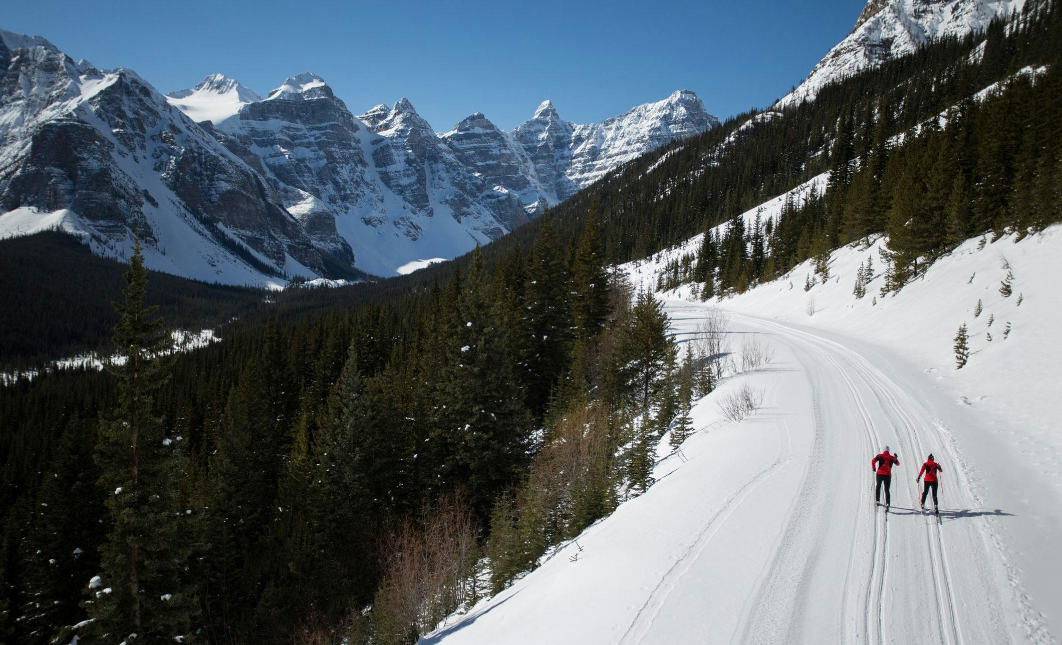 Two cross-country skiers heading up Moraine Lake Road with mountains surrounding them