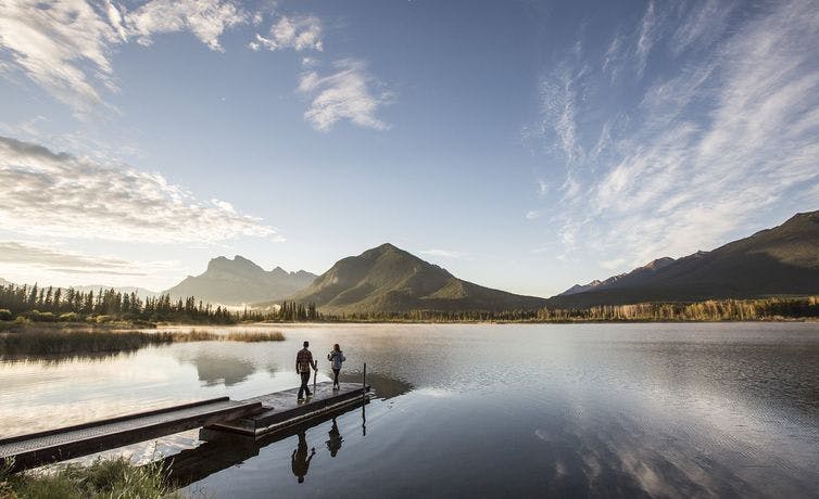 Two people walk onto a dock at Vermilion Lakes in Banff National Park.