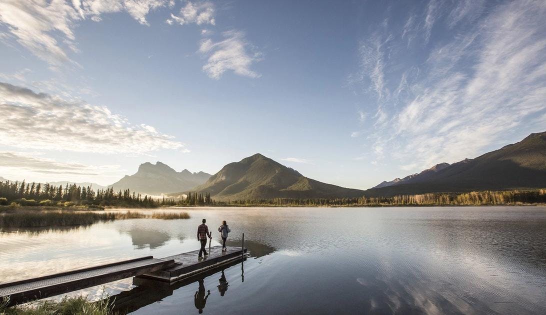Two people walk onto a dock at Vermilion Lakes in Banff National Park.
