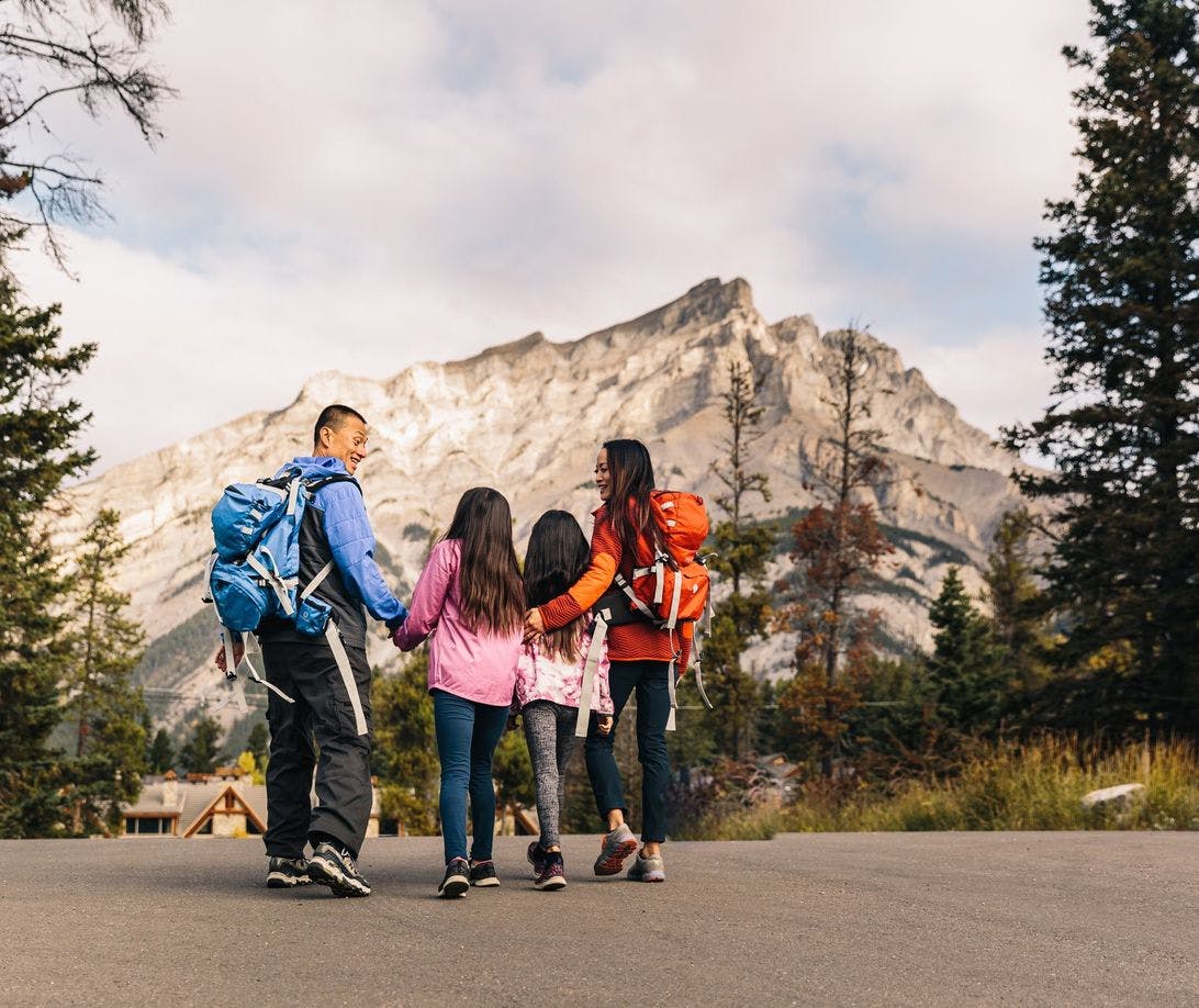 Family of four dressed for a hike and carrying backpacks walk towards Cascade Mountain