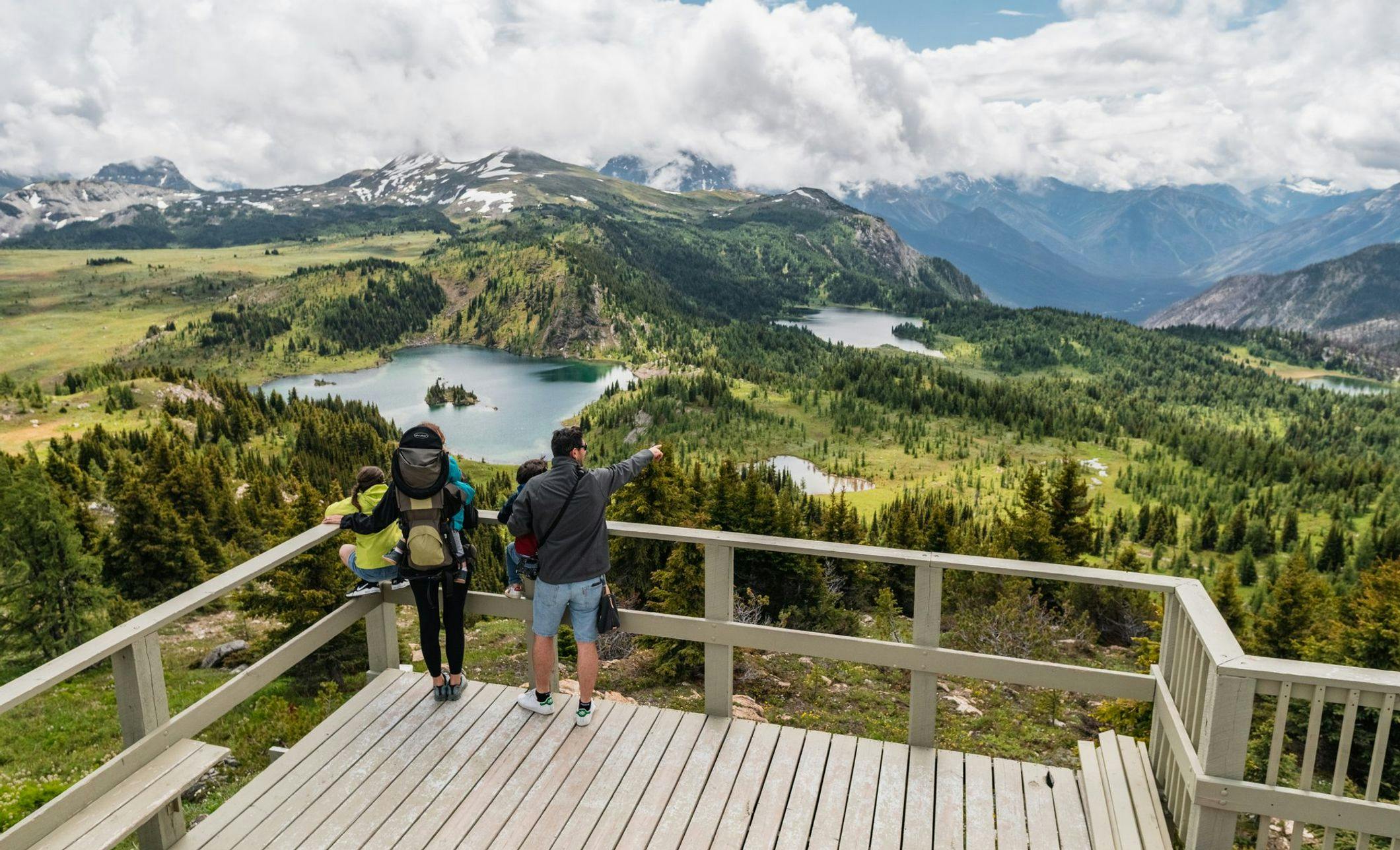 A family stands on the edge of a sightseeing platform overlooking stunning blue lakes and mountains in the alpine