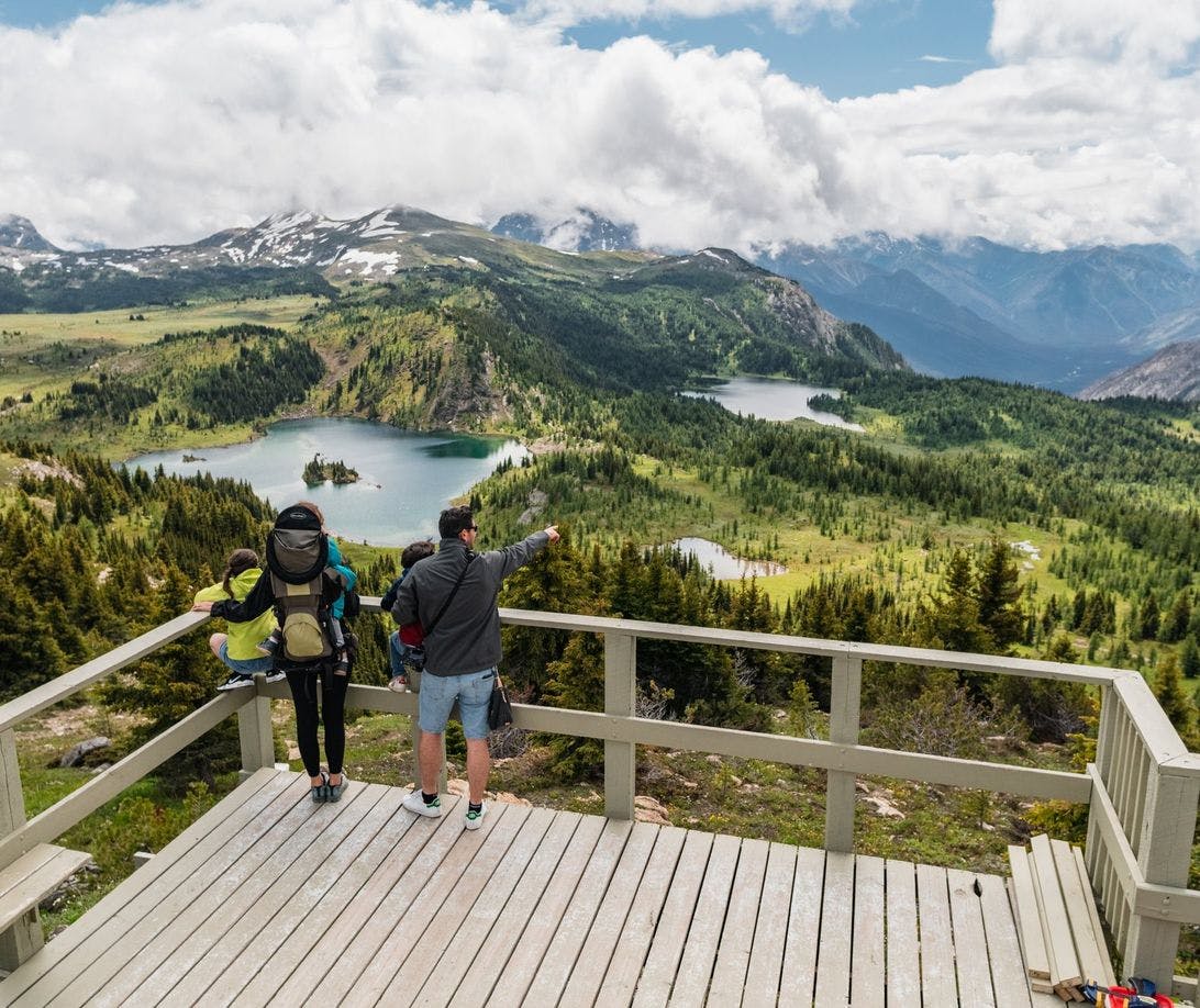A family stands on the edge of a sightseeing platform overlooking stunning blue lakes and mountains in the alpine