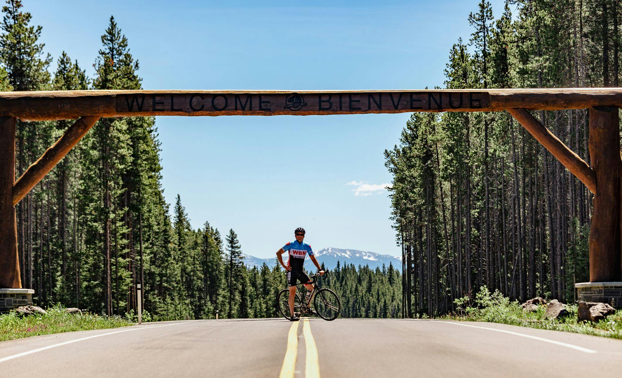 Cyclists mounted on bike underneath the Welcome sign on the Bow Valley Parkway