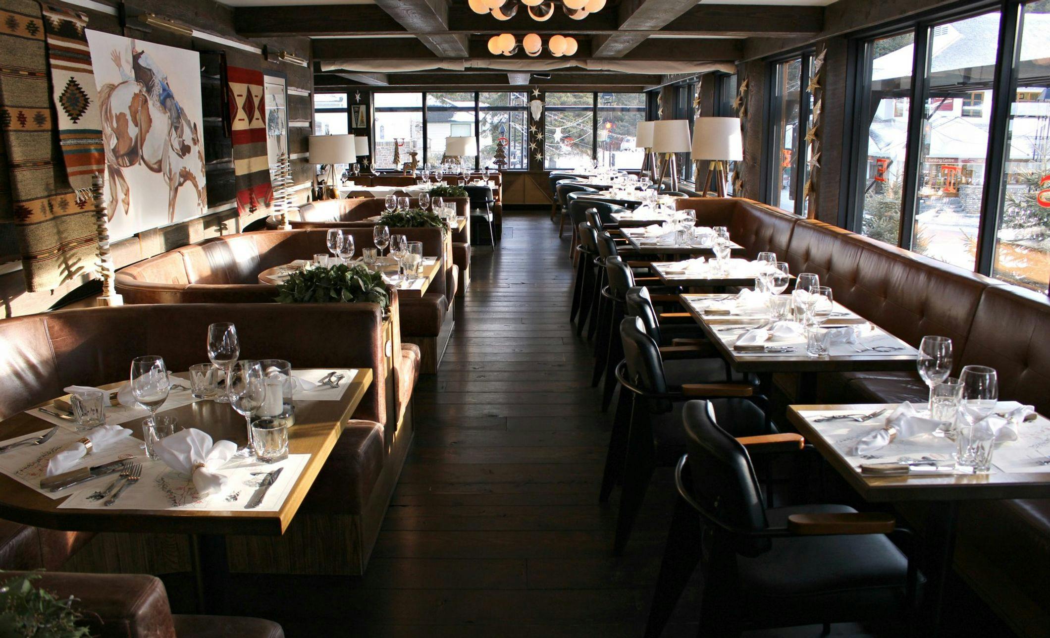 A restaurant interior with tables set for dinner and snowy rooftops outside the windows