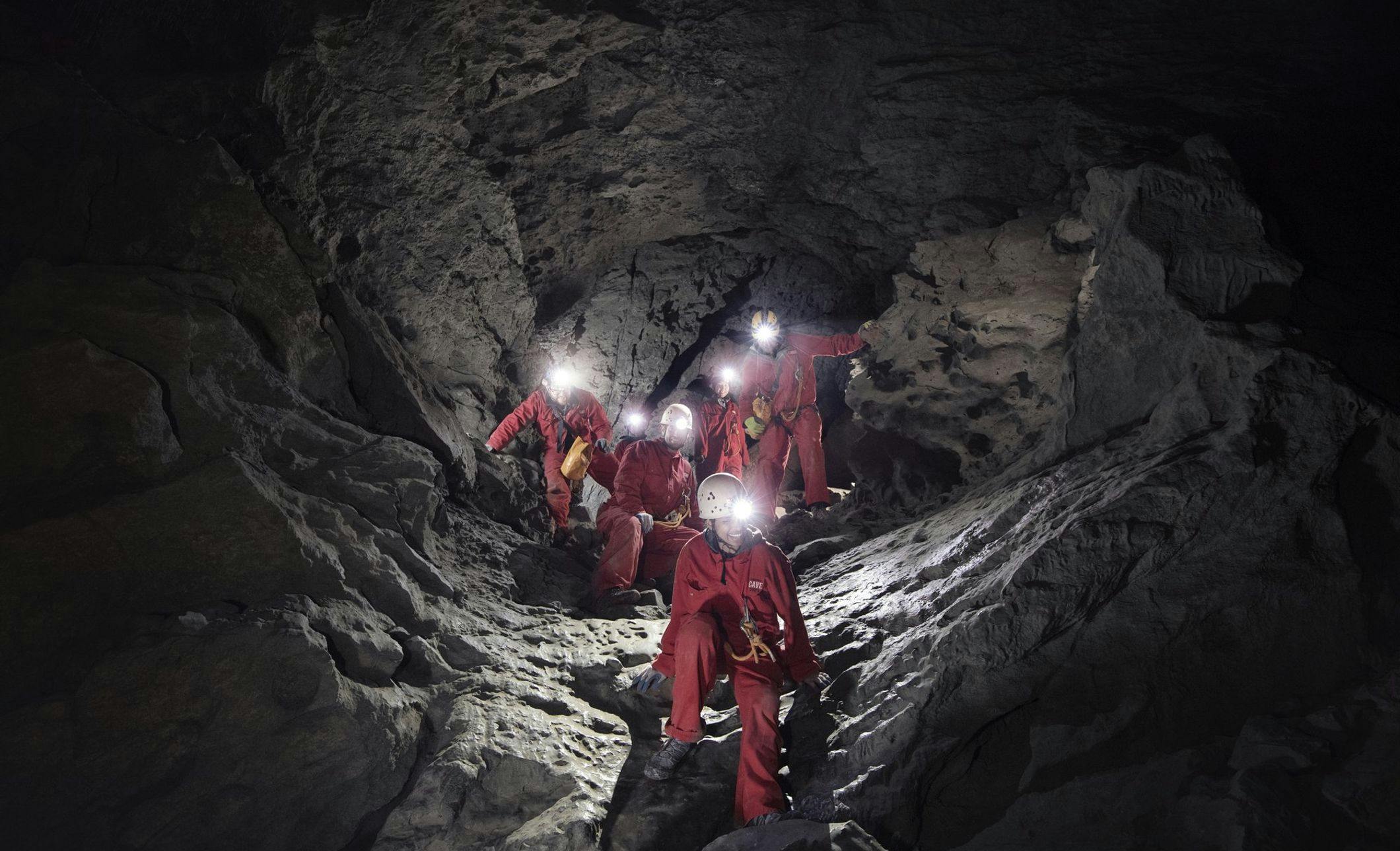 A group traveling through an underground cave wearing helmets and headlamps