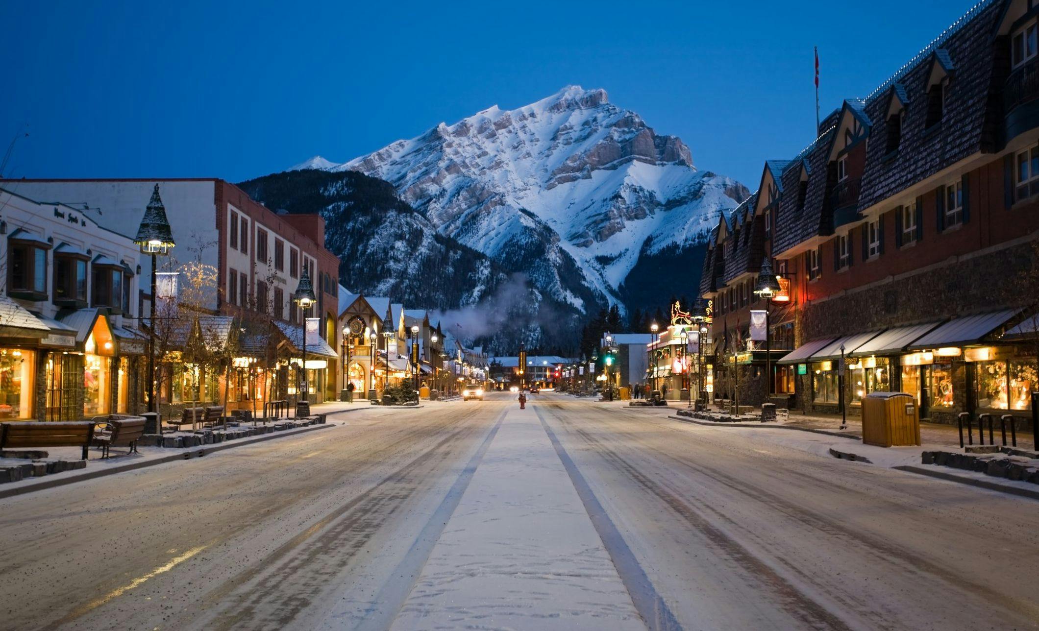 Banff Avenue at night with shop lights on and Cascade Mountain in the background