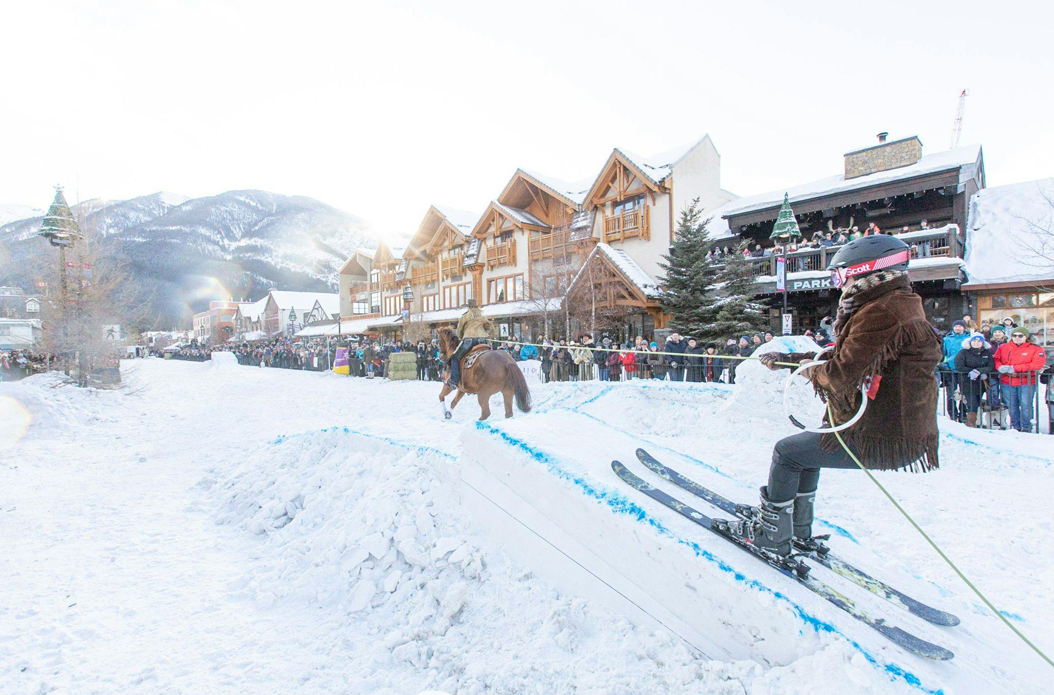 A horse pulls a trick skier over a snow jump in a Skijoring event on Banff Ave in Banff, Canada.