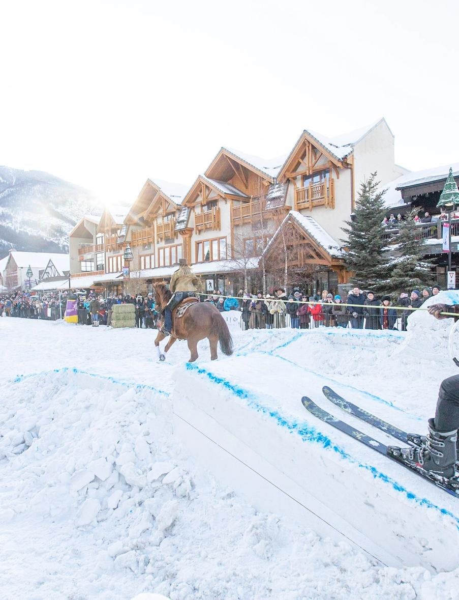 A horse pulls a trick skier over a snow jump in a Skijoring event on Banff Ave in Banff, Canada.