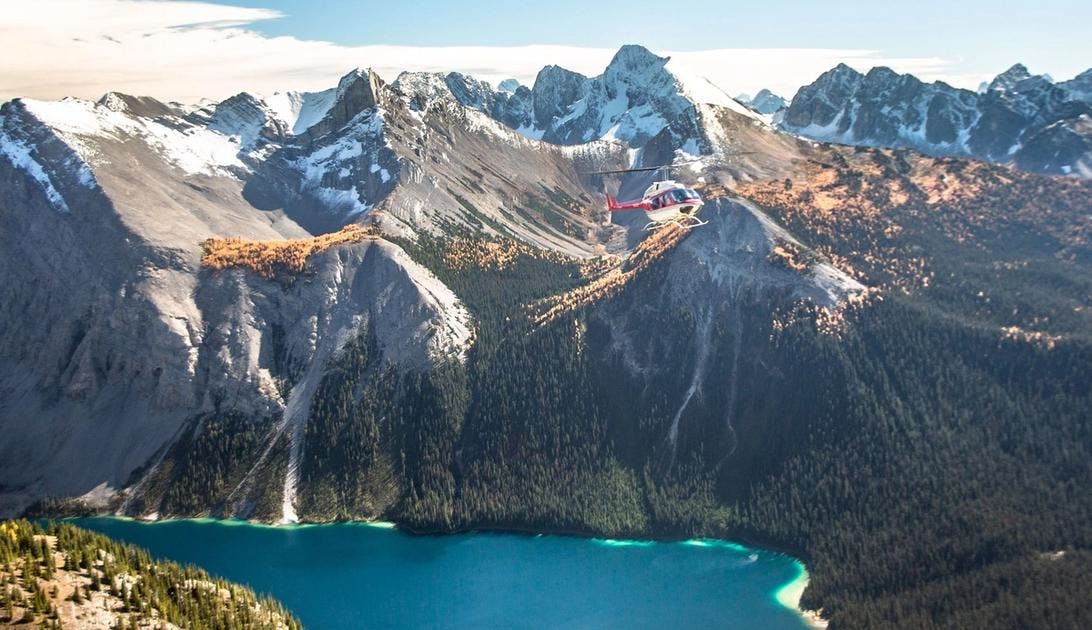 Helicopter flying over a blue lake and orange larch trees