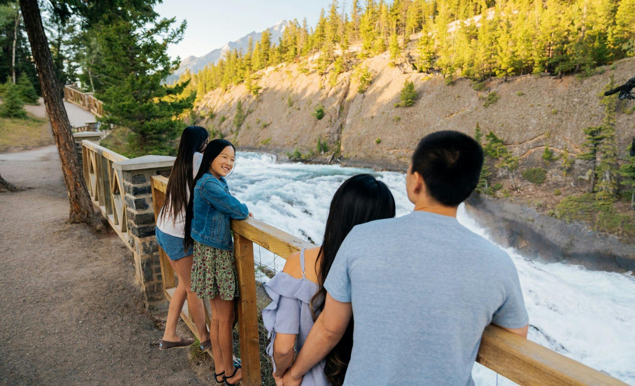 A family of four stand at a viewing platform overlooking a waterfall on a warm summer evening